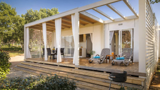 Modern Park Riviera EVO lodge with covered terrace, outdoor dining set, loungers, and tranquil setting.