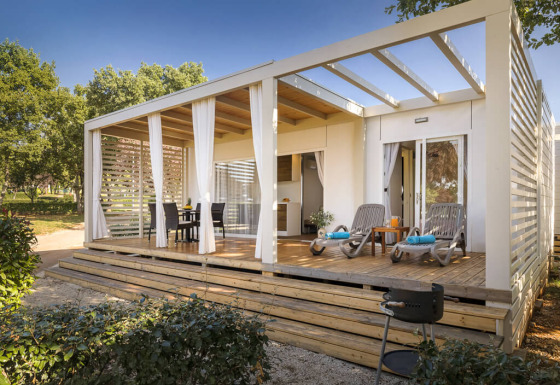 Lodge moderne Park Riviera EVO avec terrasse couverte, mobilier de jardin et transats dans un cadre vert.