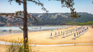 Strand met parasols en ligstoelen bij Lopar, Kroatië, met heuvels en bomen op de achtergrond.