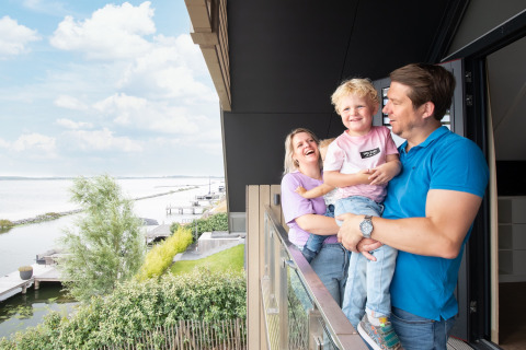 Gezin lacht en geniet op het balkon van Oesterdam Resort in Zeeland, Nederland met uitzicht op het water.