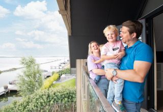 Gezin lacht en geniet op het balkon van Oesterdam Resort in Zeeland, Nederland met uitzicht op het water.