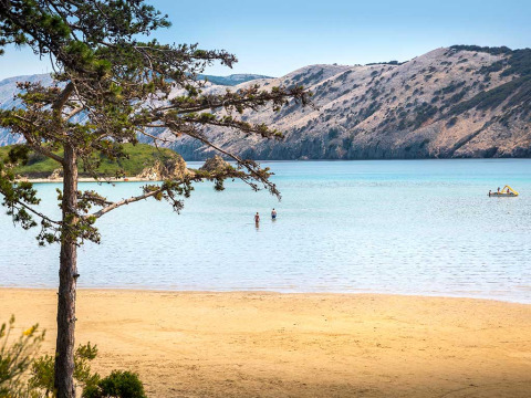 Spiaggia sabbiosa con acqua azzurra e colline al Valamar Camping San Marino, Croazia.
