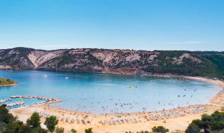 Zandstrand en rustige baai vlakbij Lopar in Primorje-Gorski Kotar, Kroatië, met heuvels en bossen.
