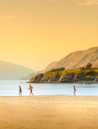Strand bij Lopar, Kroatië, met drie mensen op het zand, rustgevend water en heuvels op de achtergrond.