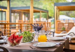 Table extérieure dans un lodge avec pastèque, salade, jus et verres, prête pour un repas d'été.