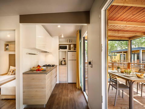 Cocina moderna de lodge con acceso a terraza cubierta, mesa de comedor exterior y vista a otras cabañas.