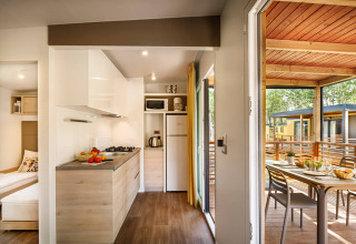 Cocina moderna de lodge con acceso a terraza cubierta, mesa de comedor exterior y vista a otras cabañas.