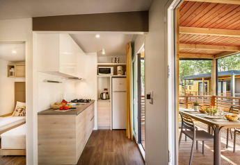 Cucina moderna di lodge con porta aperta su terrazza coperta, tavolo da pranzo e vista su altri bungalow.
