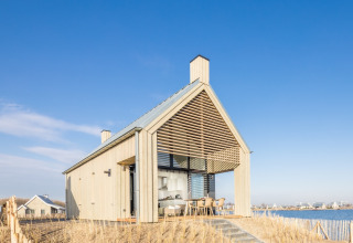 Modern vakantiehuis bij Oesterdam Resort in Zeeland, Nederland, aan het water met blauwe lucht.