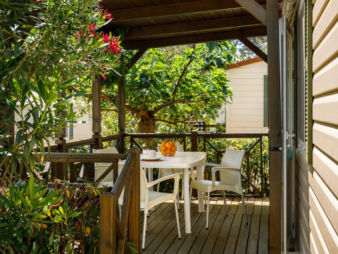 Terraza cubierta de madera con sillas y mesa blancas entre vegetación en Valamar Camping San Marino, Croacia.