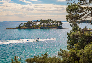 Udsigt over det klare blå hav ved Banjol, Kroatien, med en frodig ø og jetskiere i bevægelse på vandet.