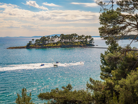 Vista sul mare azzurro di Banjol, Croazia, con un'isola verdeggiante e moto d'acqua che sfrecciano.