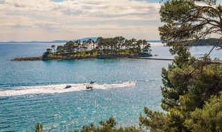 View of the sparkling blue sea in Banjol, Croatia, featuring a lush island and jet skiers racing by.