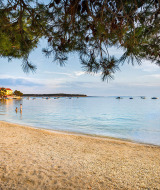 Peaceful beach with calm sea, boats, and pine branches near Banjol, Primorje-Gorski Kotar, Croatia.
