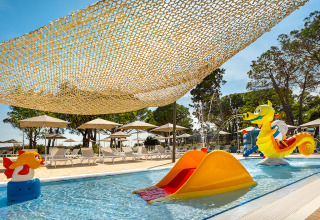 Family pool area with water slide, lounge chairs, parasols and seahorse at Valamar Camping Padova in Croatia.