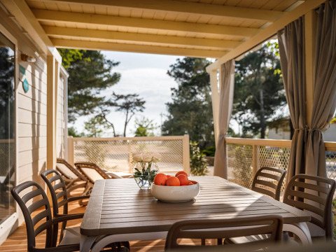Terraza cubierta en Marine Home lodge con mesa, sillas, tumbonas y un bol de naranjas en la mesa.