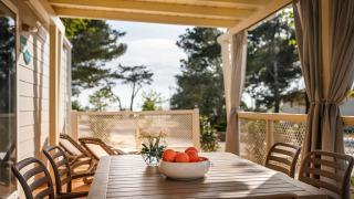 Terraza cubierta en Marine Home lodge con mesa, sillas, tumbonas y un bol de naranjas en la mesa.