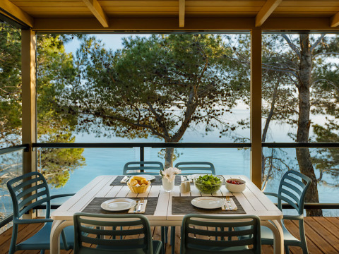 Mesa de comedor al aire libre para cuatro personas con vistas al mar y pinos en Valamar Camping Padova, Croacia.