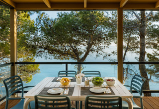 Outdoor dining table set for four on a terrace with sea view and pine trees at Valamar Camping Padova, Croatia.