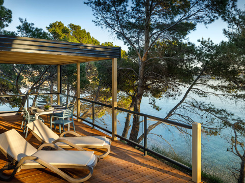 Solterrasse med liggestole og spisebord på Valamar Camping Padova, omgivet af fyrretræer og havudsigt.