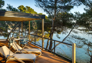 Terraza con tumbonas y mesa de comedor en Valamar Camping Padova, rodeada de pinos y vistas al mar.
