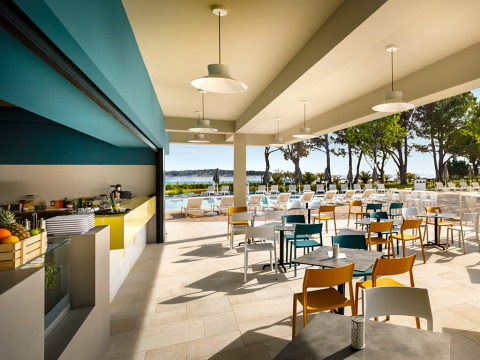 Espace de restauration extérieur au Valamar Camping Padova en Croatie, avec tables, chaises, piscine et vue sur la mer.