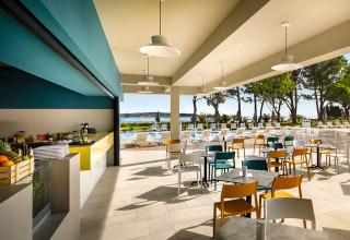 Zona de restaurante al aire libre en Valamar Camping Padova, Croacia, con mesas, sillas, piscina y vistas al mar.