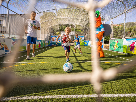 Children play soccer with an adult and a mascot on a fenced field at Valamar Camping Padova, Croatia.