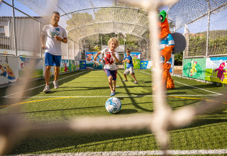 Niños juegan fútbol con un adulto y una mascota en el campo de Valamar Camping Padova en Croacia.
