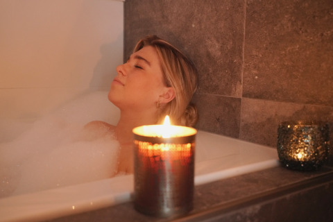 Vrouw ontspant in een bubbelbad met brandende kaars, luxueuze sfeer bij Oesterdam Resort in Zeeland.