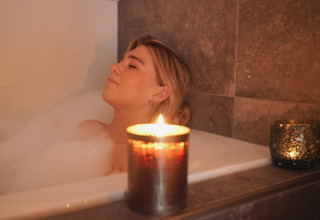 Vrouw ontspant in een bubbelbad met brandende kaars, luxueuze sfeer bij Oesterdam Resort in Zeeland.