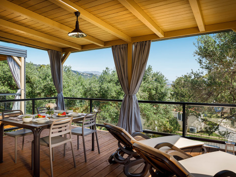 Überdachte Terrasse im Padova Suite Lodge mit Esstisch, Liegestühlen und Blick auf grüne Bäume und Berge.