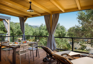 Terraza cubierta en la Padova Suite lodge con mesa de comedor, tumbonas y vistas a árboles y colinas verdes.