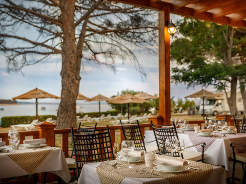 Buitenterras van Valamar Camping Padova met uitzicht op het strand en rieten parasols in Kroatië.
