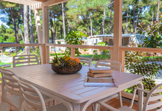 Terraza al aire libre con mesa y sillas blancas, canasta de fruta y libros en Valamar Camping Padova, Croacia.