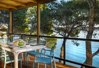 Outdoor dining area on a terrace with blue chairs and a view of trees and water at Valamar Camping Padova.