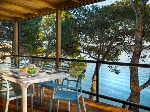 Zona de comedor exterior en terraza con sillas azules y vistas a árboles y agua en Valamar Camping Padova.