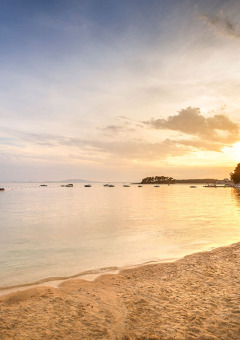 Sunset on the beach at Valamar Camping Padova with lounge chairs, parasol, and boats floating on calm water.