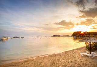 Solnedgang over stranden ved Valamar Camping Padova med liggestole, strandparaply og både på vandet i Kroatien.
