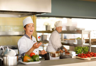 Two chefs in uniform are preparing food in a bright, modern kitchen with fresh vegetables on the counter.