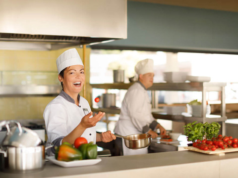 Two chefs in uniform are preparing food in a bright, modern kitchen with fresh vegetables on the counter.