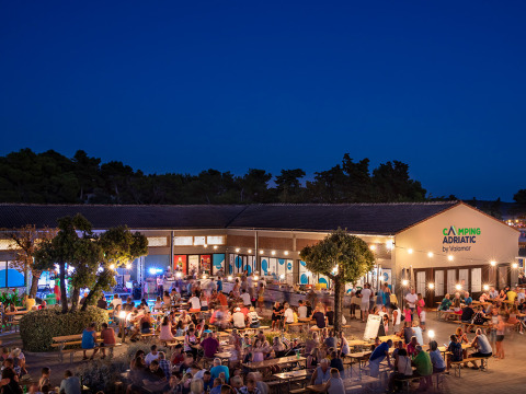 Aftenscene ved Valamar Camping Padova, hvor gæster hygger sig udendørs under oplyste træer i Kroatien.