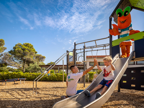 Niño se desliza en el tobogán y choca la mano con un adulto en Valamar Camping Padova, Croacia.