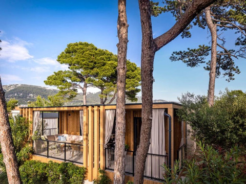 Hilltop Green Home lodge surrounded by lush trees and mountains, under a clear blue sky on a sunny day.