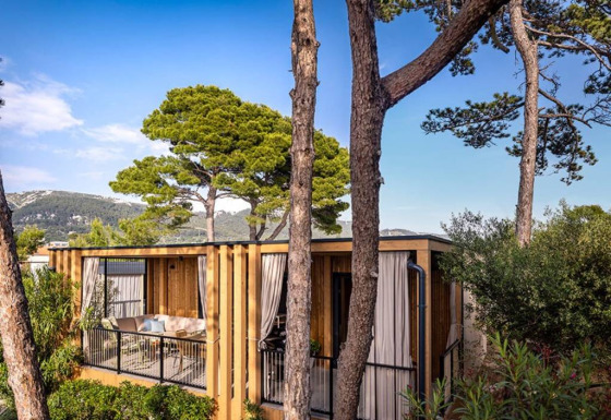 Hilltop Green Home lodge surrounded by lush trees and mountains, under a clear blue sky on a sunny day.