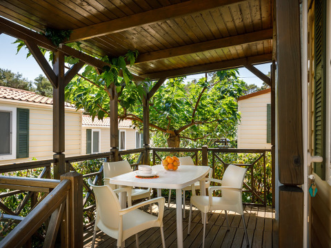 Terraza cubierta en la cabaña Padova Home con mesa blanca, cuatro sillas y naranjas bajo árboles frondosos.