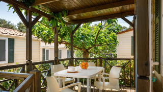 Terraza cubierta en la cabaña Padova Home con mesa blanca, cuatro sillas y naranjas bajo árboles frondosos.
