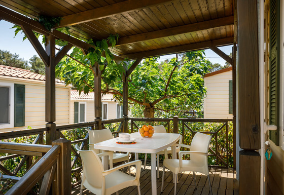Terraza cubierta en la cabaña Padova Home con mesa blanca, cuatro sillas y naranjas bajo árboles frondosos.