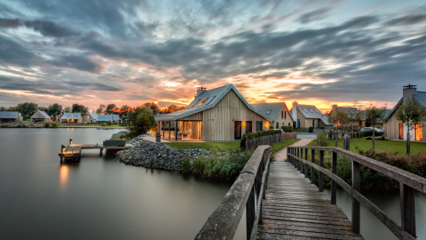 Houten brug bij zonsondergang naar vakantiehuisjes aan het water in Oesterdam Resort, Zeeland, Nederland.