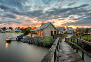 Houten brug bij zonsondergang naar vakantiehuisjes aan het water in Oesterdam Resort, Zeeland, Nederland.